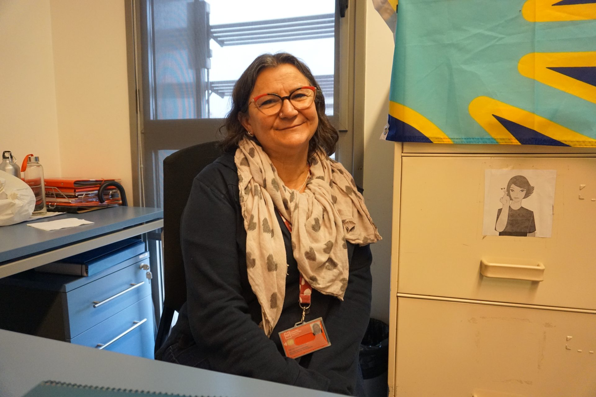 La professora i investigadora Delfina Aliaga, al seu despatx. A la dreta, de la part superior de l'armariet, penja la bandera de les persones sordes Imatge inicial - La professora i investigadora Delfina Aliaga, al seu despatx. A la dreta, de la part superior de l'armariet, penja la bandera de les persones sordes